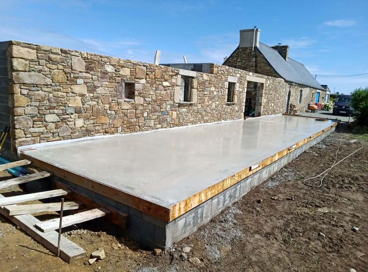 Dalle de béton à côté d'une maison en pierre en construction.