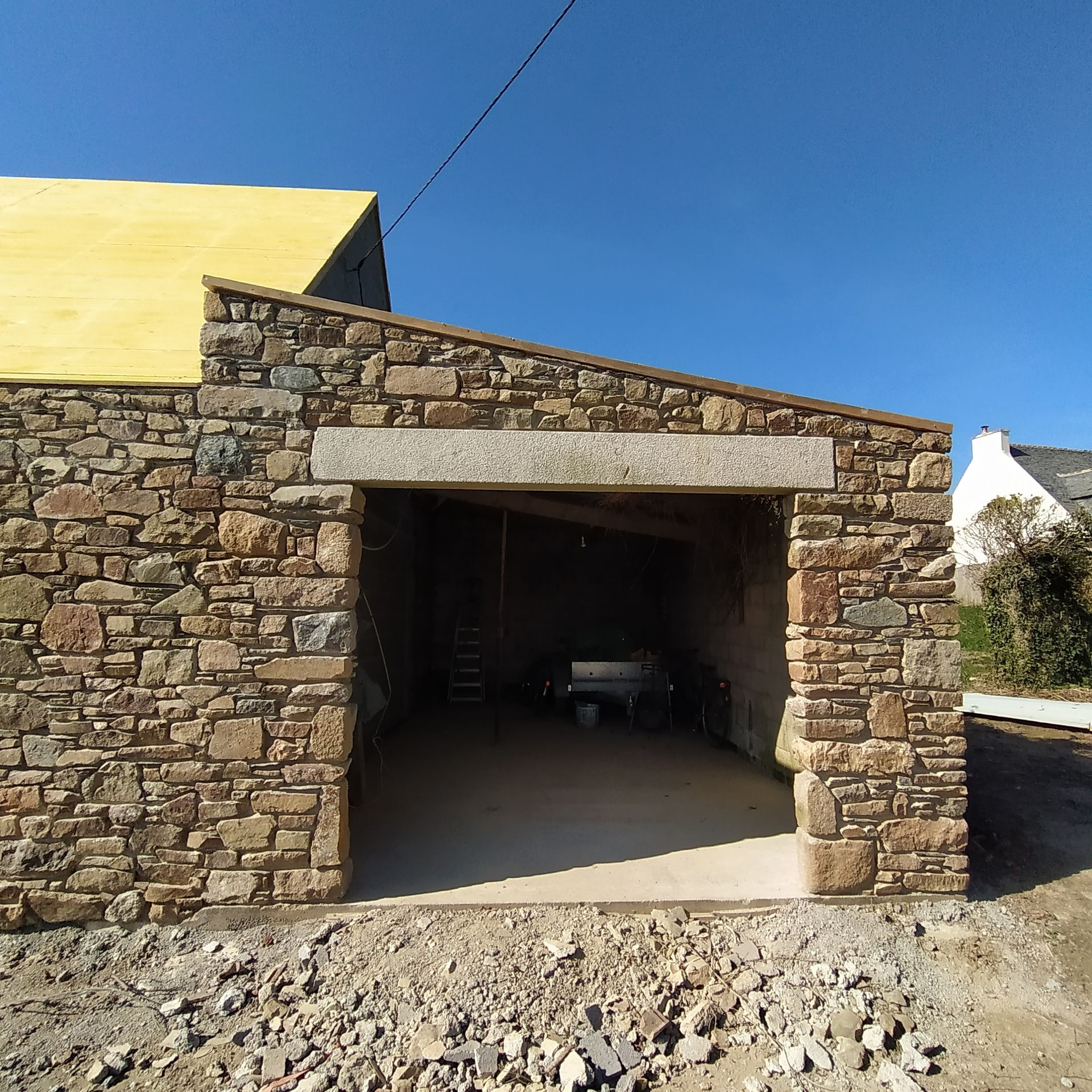 Entrée de garage en pierre avec porte ouverte, gravats devant.