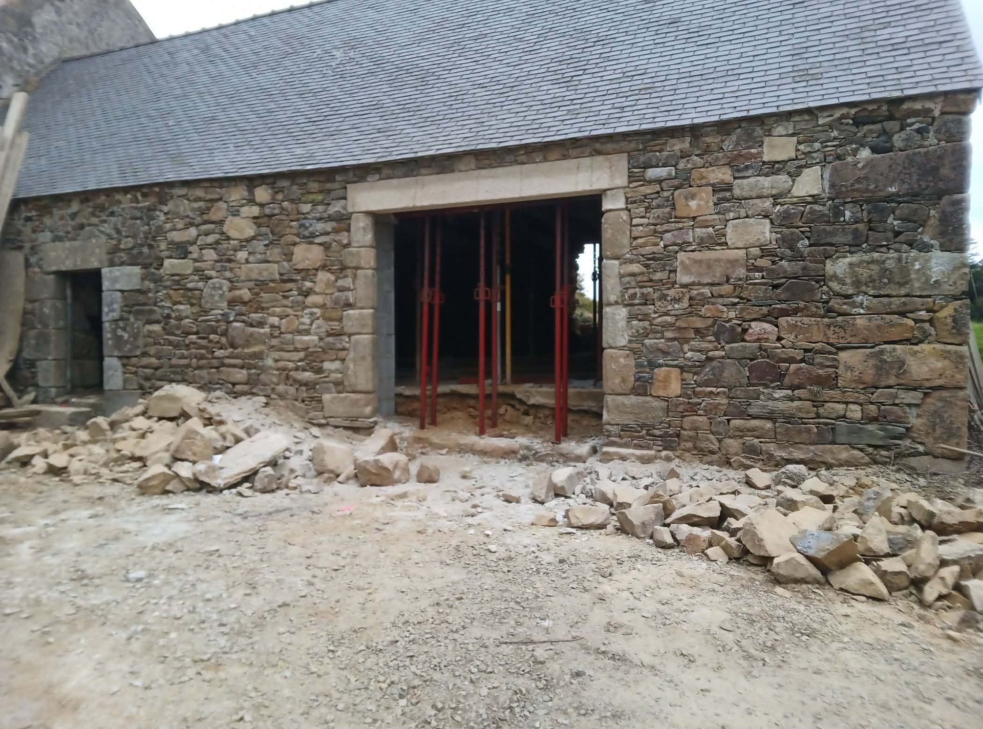 Maison en pierre avec de grandes portes coulissantes en verre et une petite terrasse.