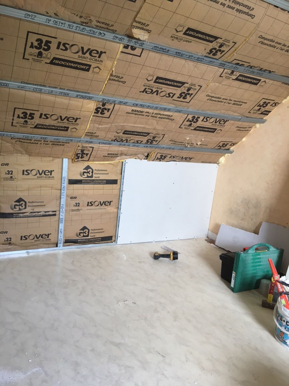 Intérieur d'un grenier en cours d'aménagement, avec isolation, plaques de plâtre et outils visibles.