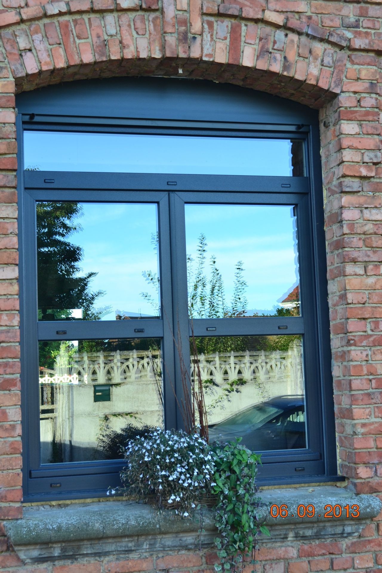 Fenêtre en briques avec verre réfléchissant, donnant sur le ciel et les environs.