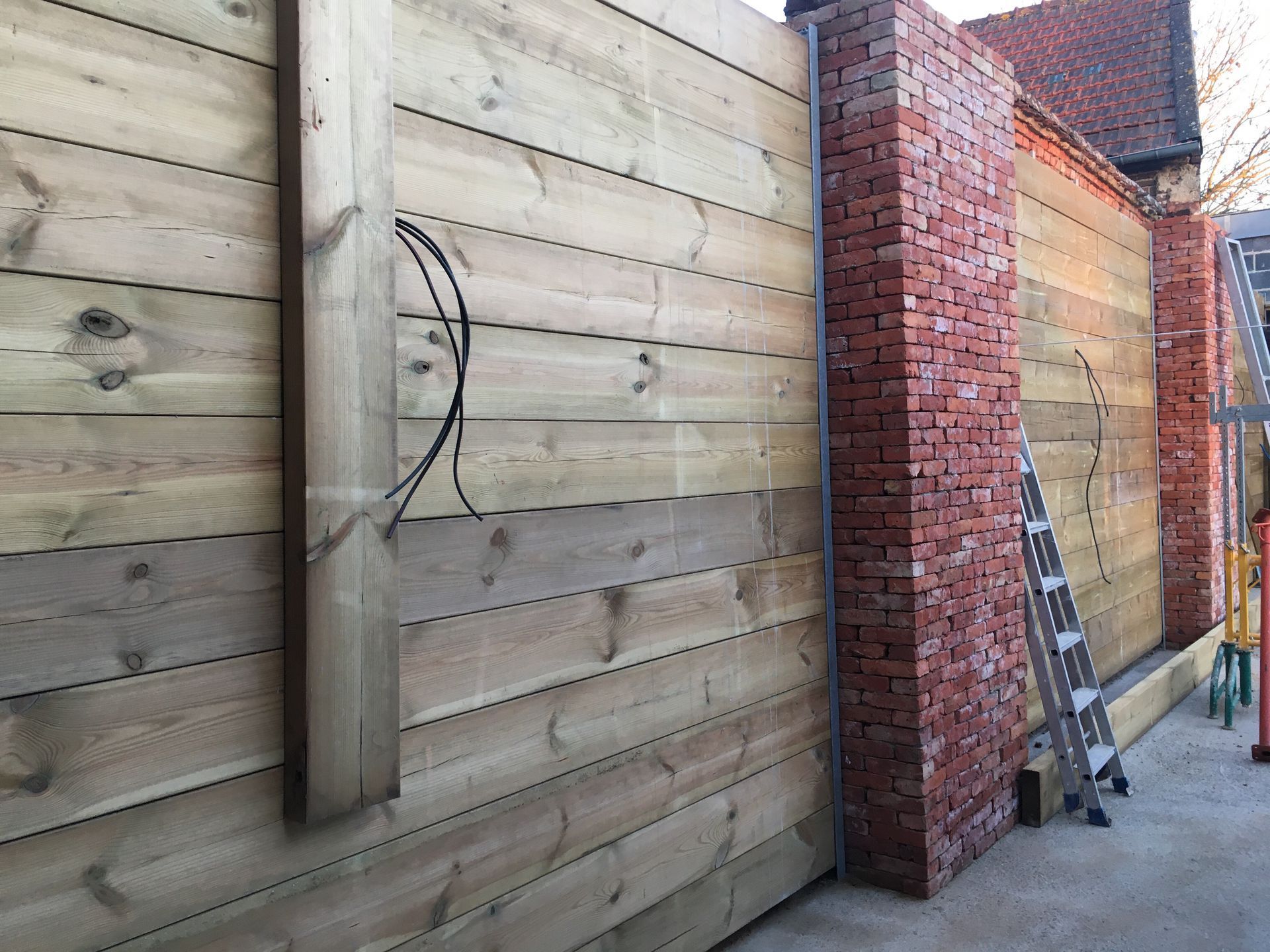 Clôture en bois avec piliers en briques, échelle et fils de fer.