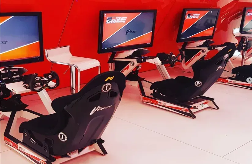 Asientos y volantes de simulador de carreras negros frente a monitores en una sala de juegos roja.