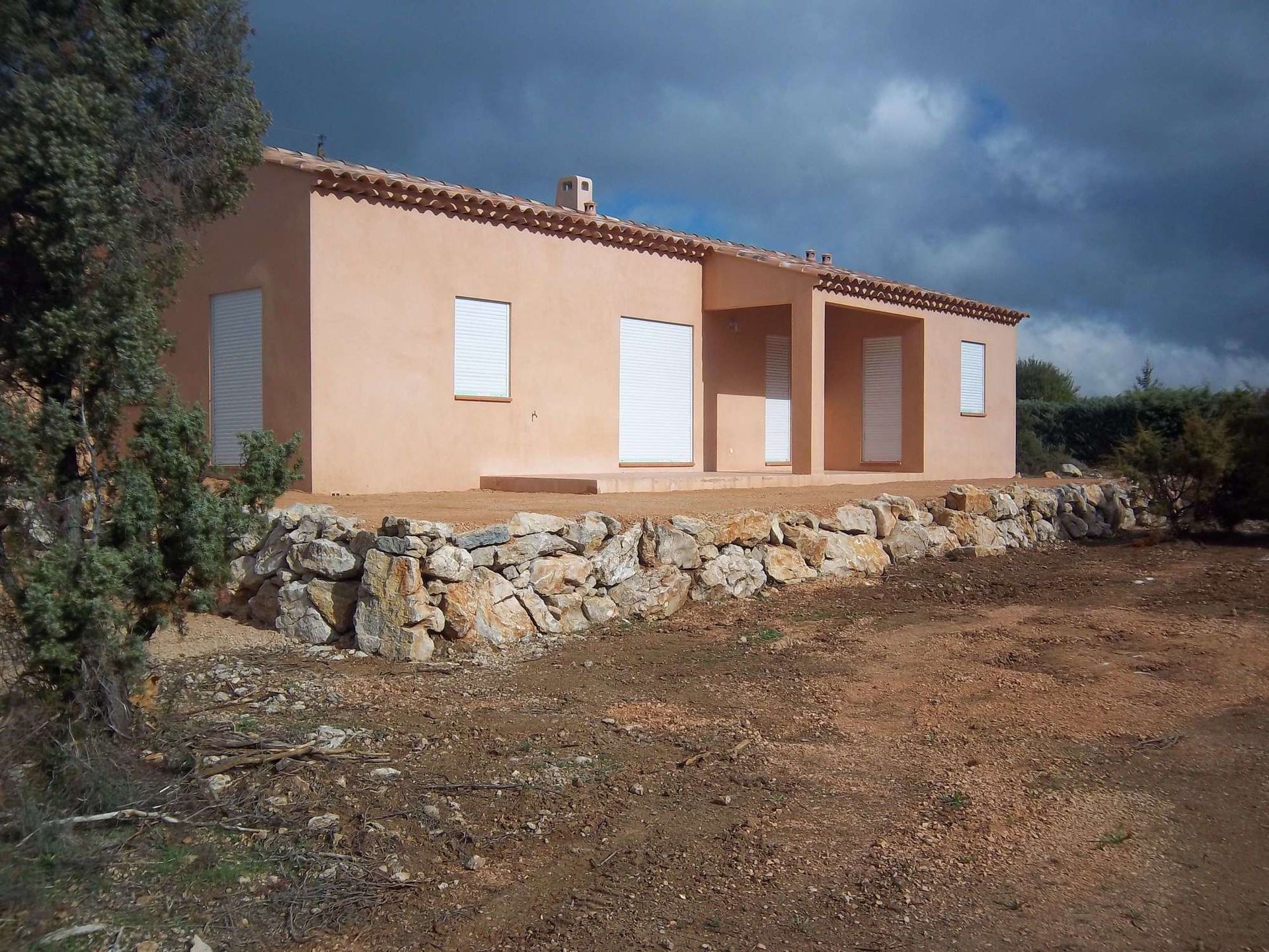 Une pelleteuse Volvo jaune sur un champ herbeux et arboré, sous un ciel bleu.