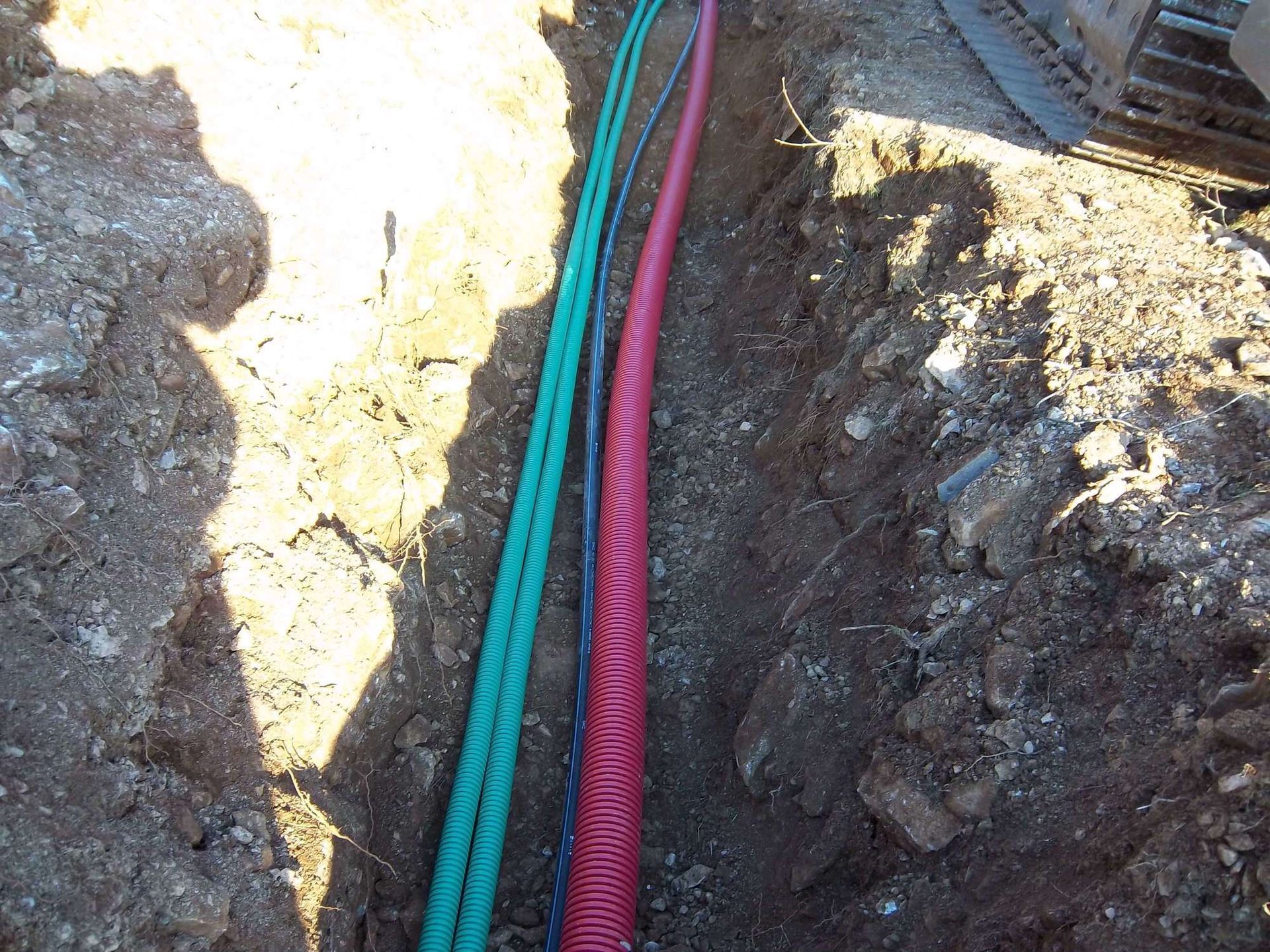 Tuyaux souterrains en PVC gris raccordés à une boîte de jonction en béton dans la terre.