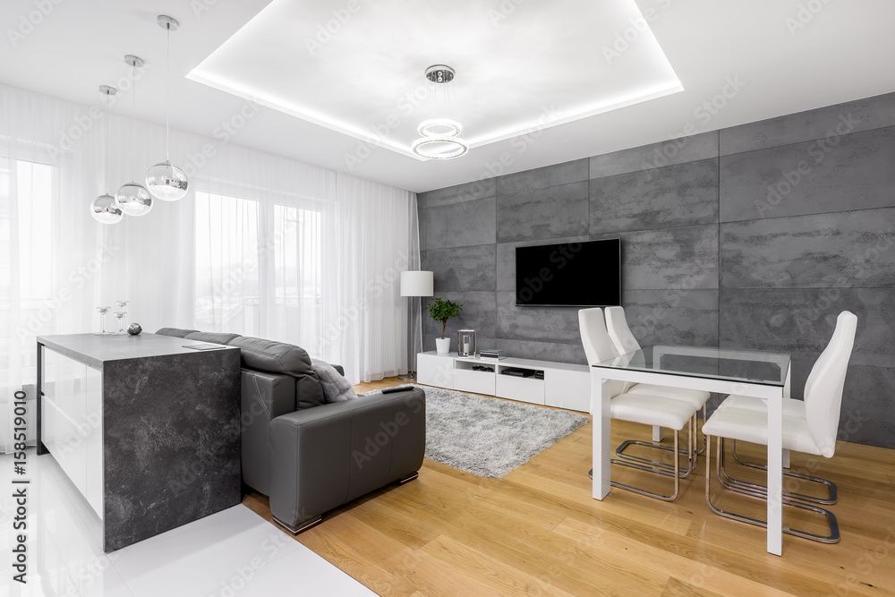 Salon moderne à aire ouverte avec canapé gris, table à manger blanche, télévision et mur d'accent carrelé