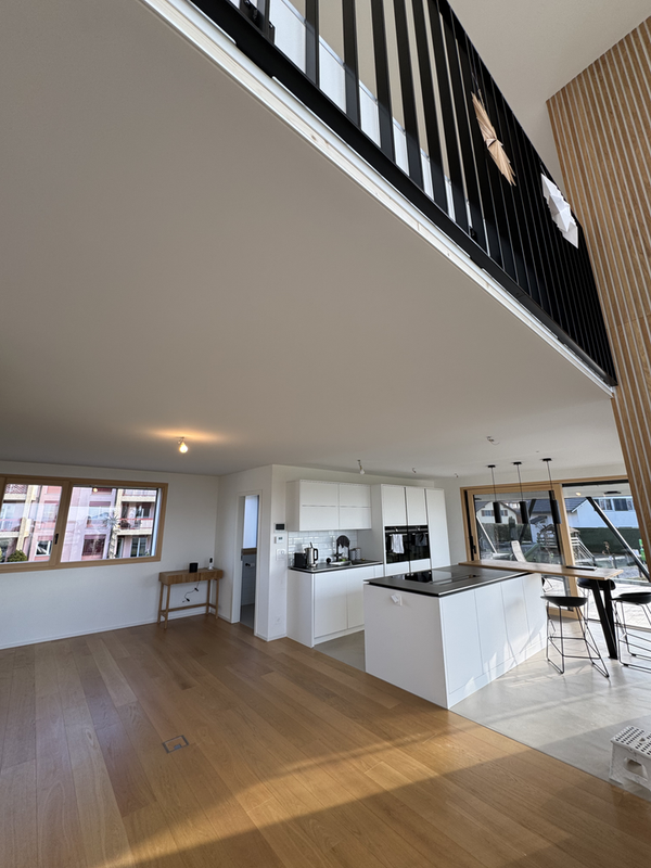 Espace de vie moderne et ouvert avec îlot de cuisine, parquet et rampe d'escalier au-dessus