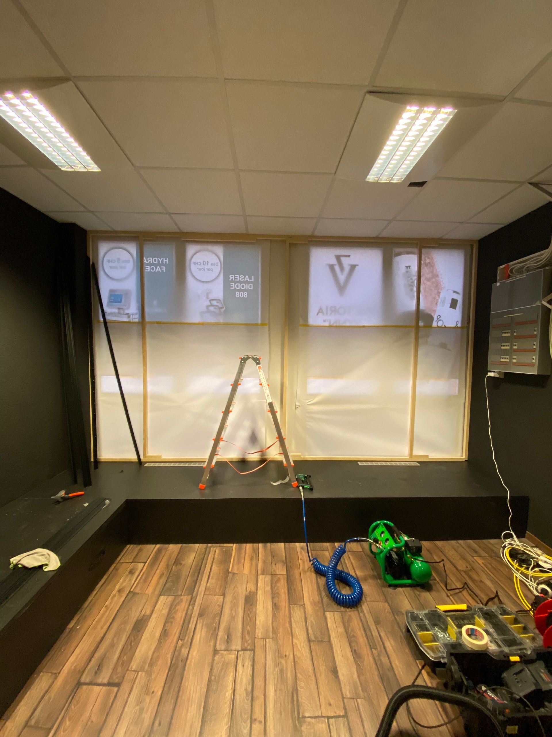 Pièce intérieure avec parquet, éclairage vif au plafond et pièces et outils de robotique éparpillés près du mur du fond.