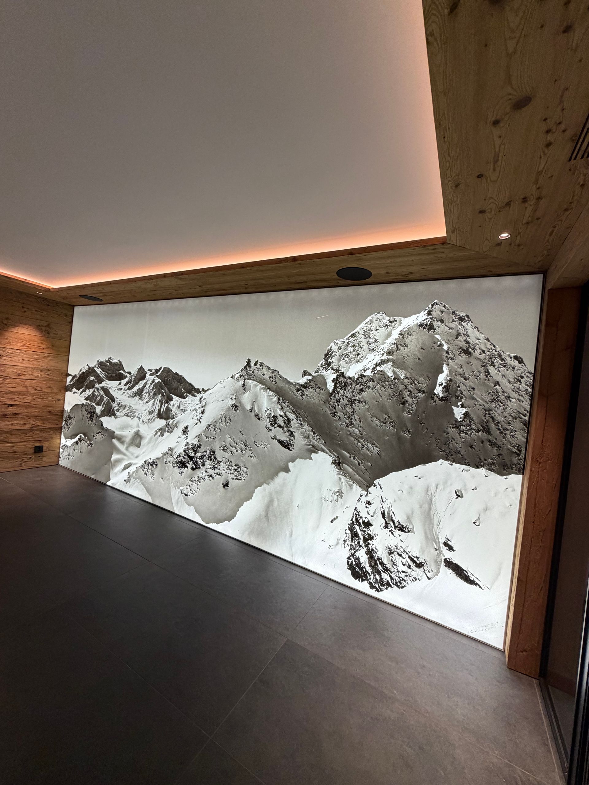 Intérieur moderne avec une grande fresque murale représentant des sommets enneigés et un éclairage chaleureux au plafond