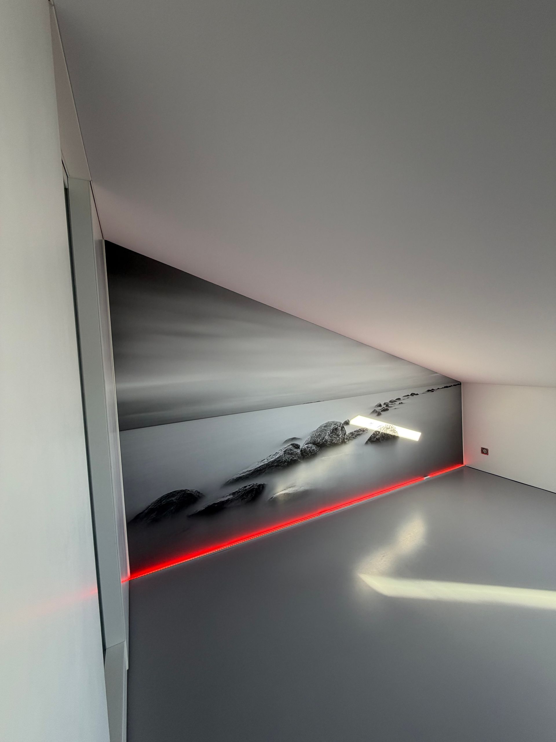 Coin intérieur minimaliste blanc avec un plafond incliné et une bande LED rouge au sol