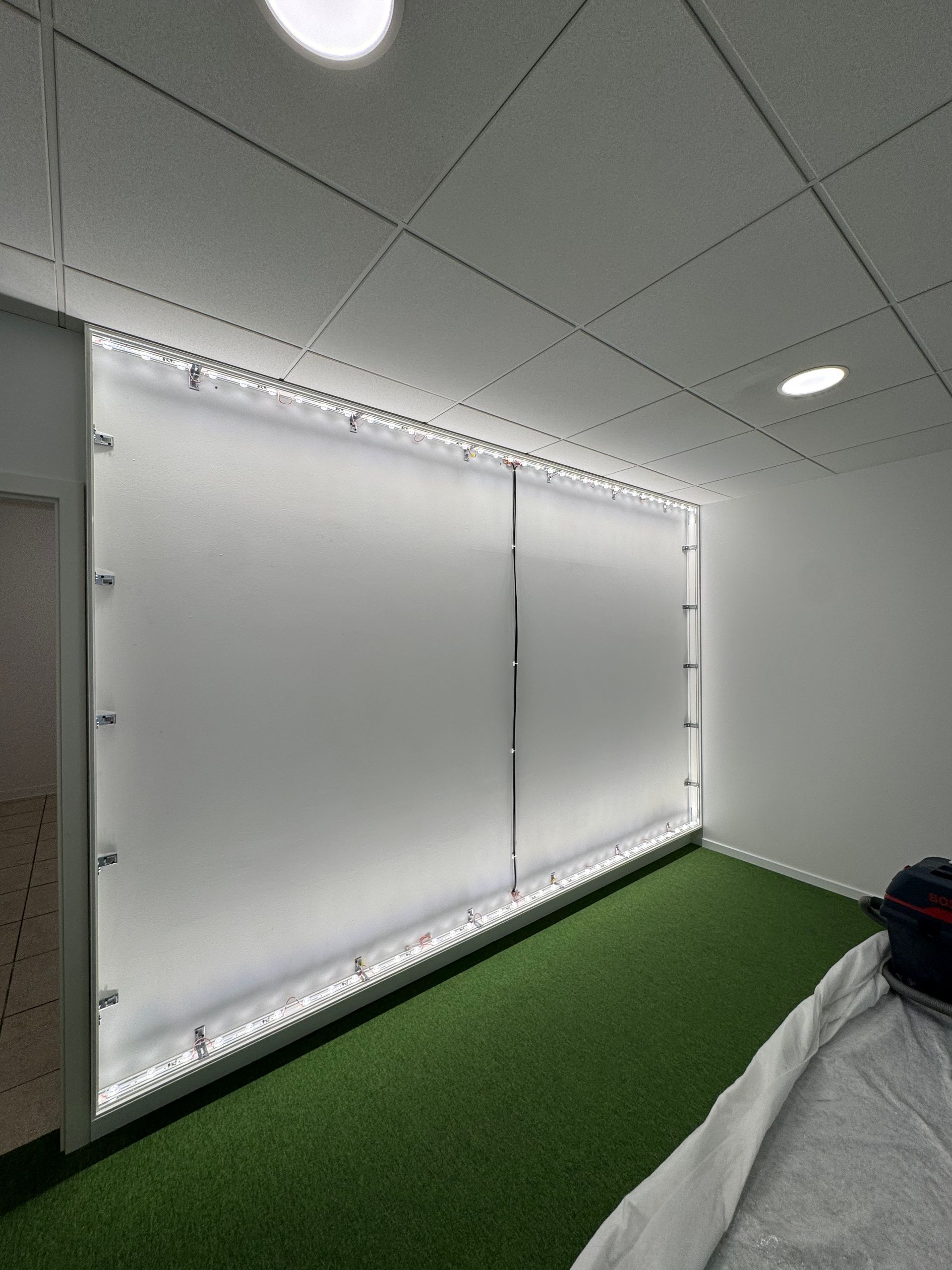 Espace de bureau vide avec moquette verte, murs blancs et un grand panneau coulissant éclairé sur la gauche.