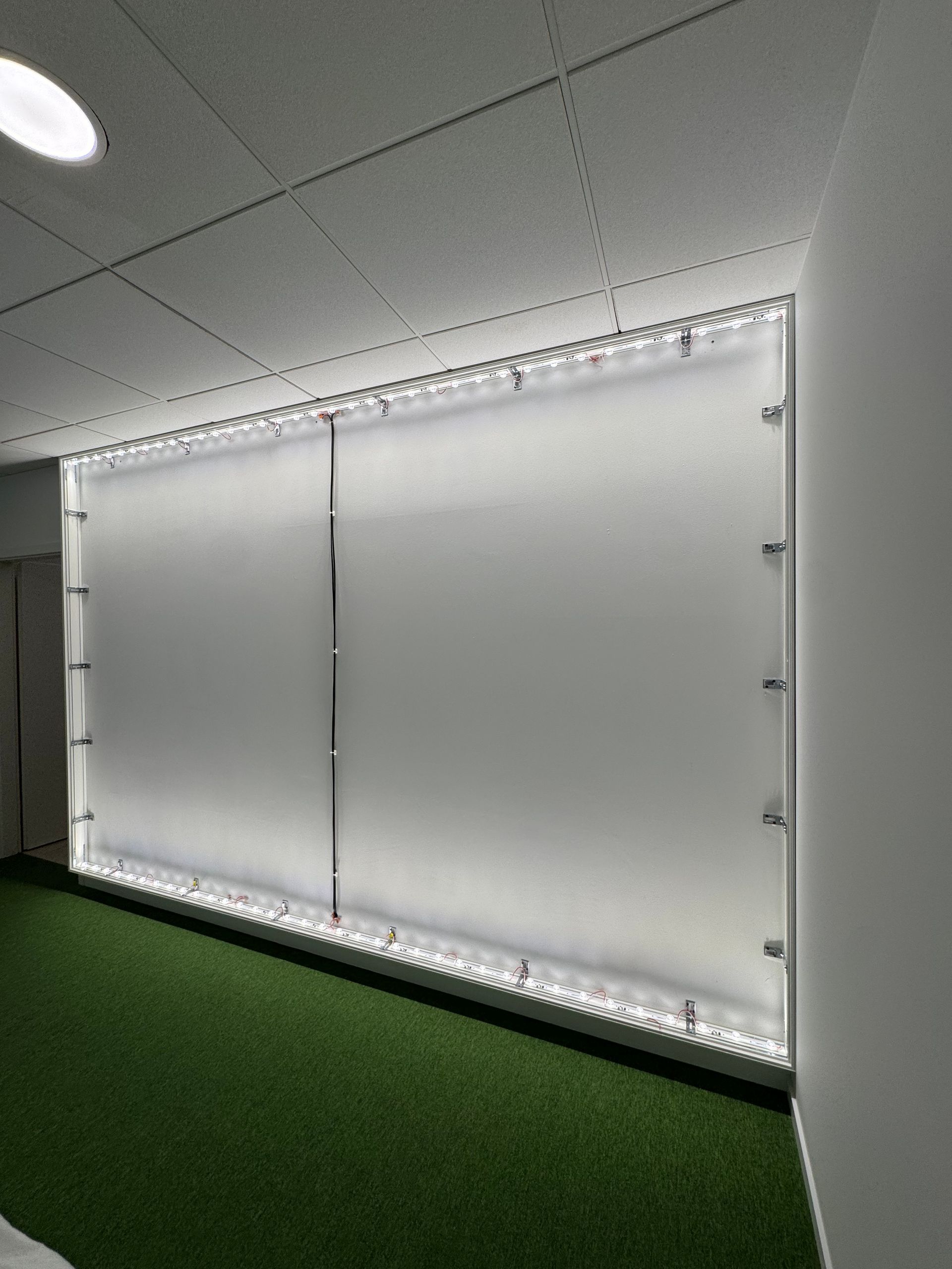 Panneaux muraux blancs translucides avec éclairage par bande LED dans une pièce au sol recouvert de moquette verte.