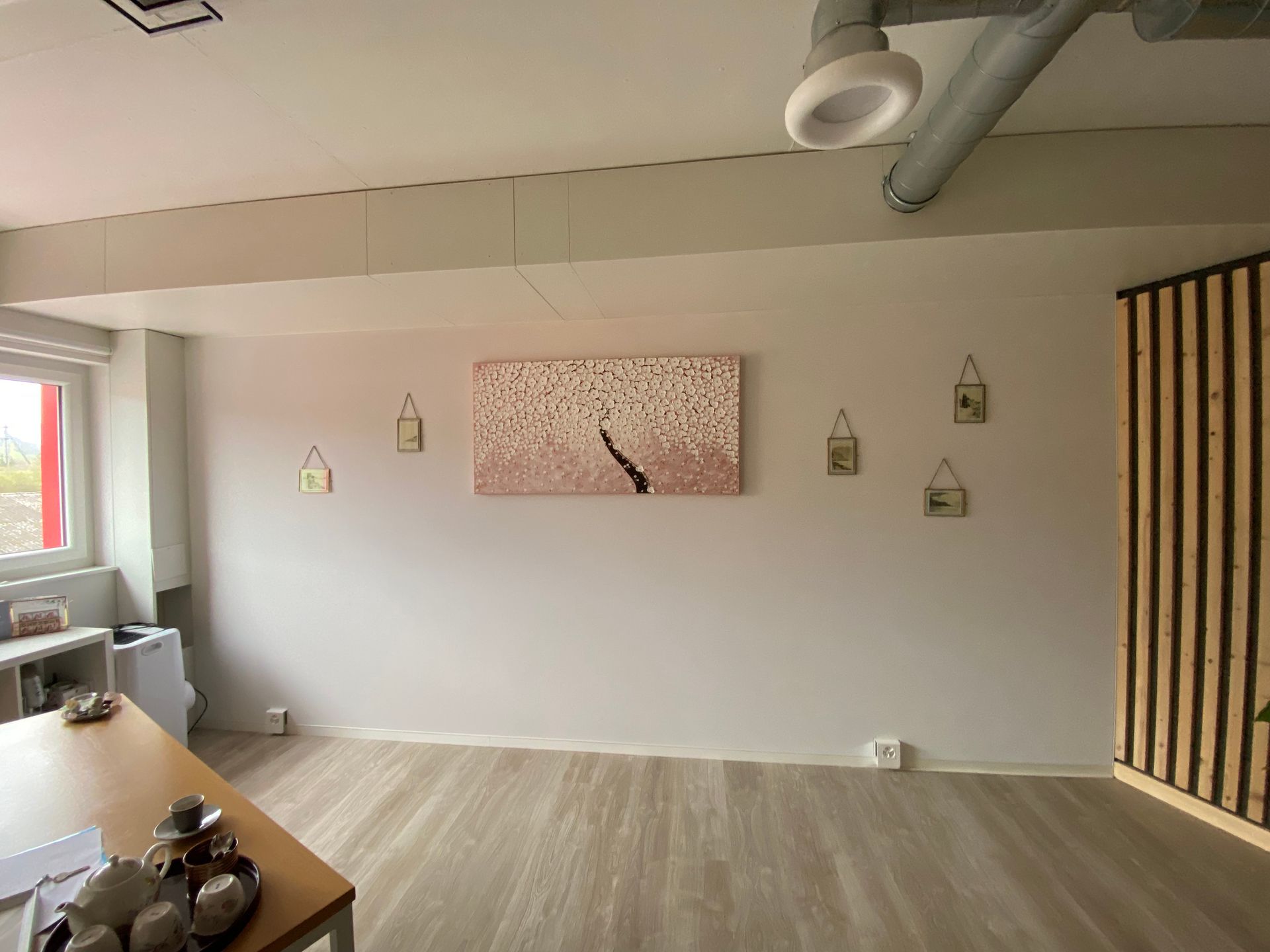 Pièce lumineuse et vide avec parquet, tableaux, petites étagères décoratives et un mur d'accent à rayures.