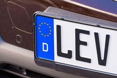 Zwei sich überlappende Kfz-Kennzeichen im EU-Stil: gelb und weiß, jeweils mit einem blauen Streifen und einem weißen „D“ auf schwarzem Hintergrund
