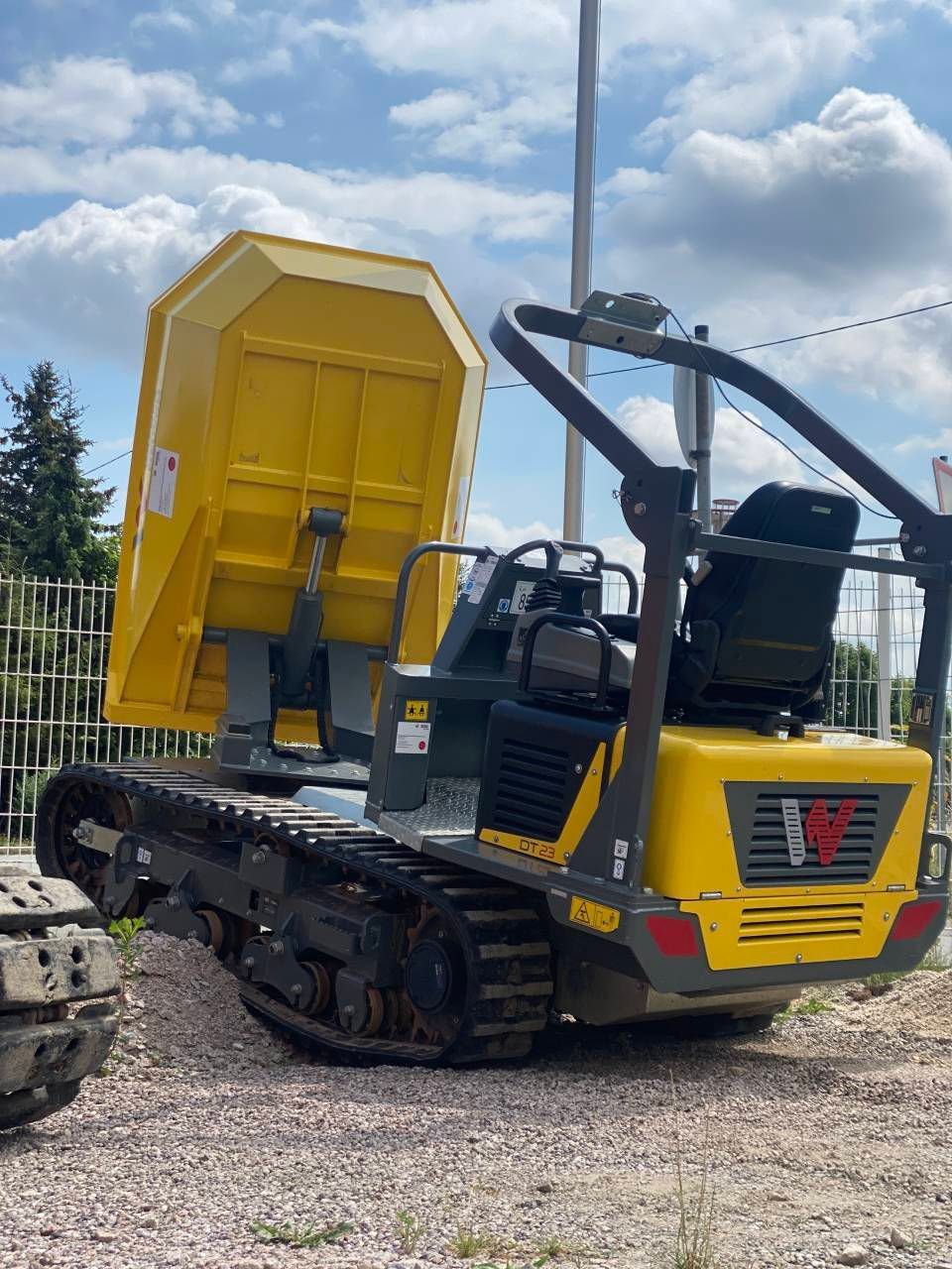 Gelber Kettenkipper mit erhöhter Ladefläche auf Kies vor bewölktem Himmel.