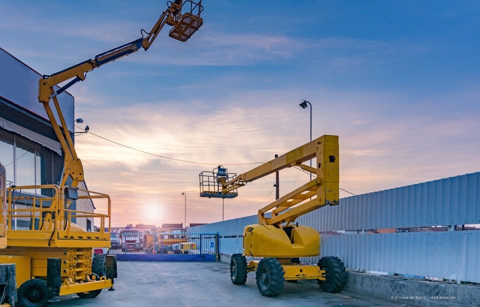 Gelbe Hubarbeitsbühnen auf einer Baustelle mit Arbeitern. Blauer Himmel und industrieller Hintergrund.