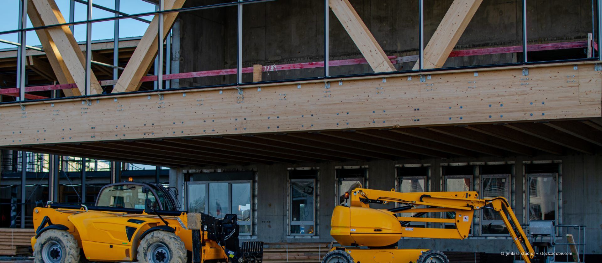 Baustelle mit gelben Maschinen und Holzbalken.