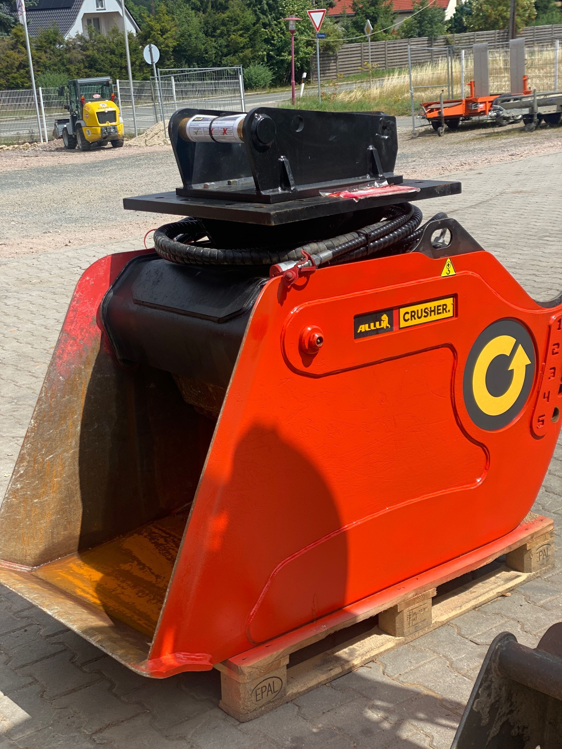 Orangefarbener Baggerlöffelaufsatz auf einer Palette, einsatzbereit im Freien.