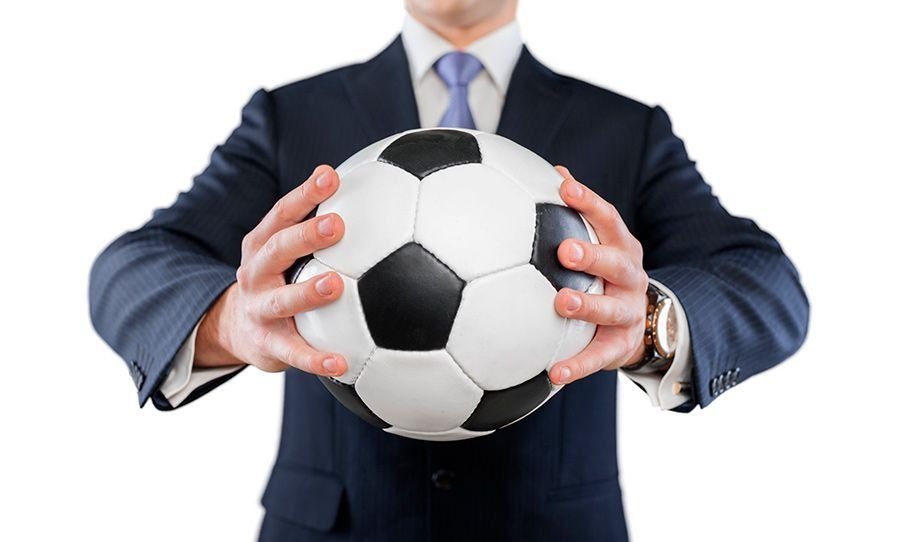 Un hombre con traje sostiene un balón de fútbol en sus manos.