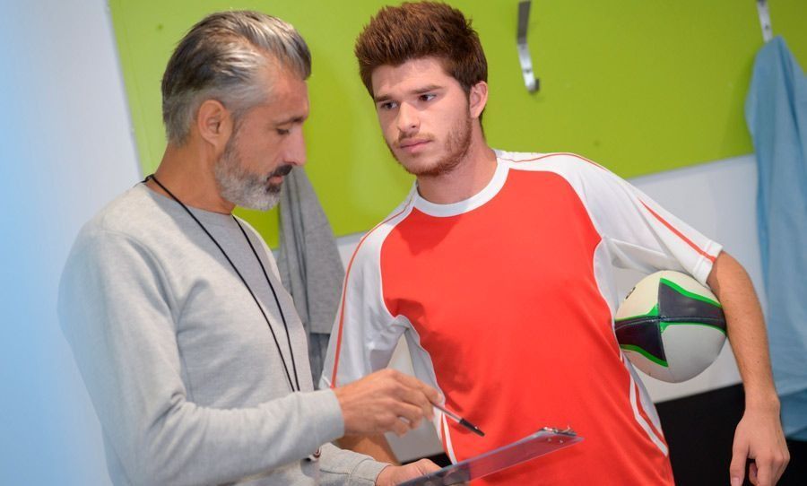 Un entrenador está hablando con un jugador de fútbol en un vestuario.