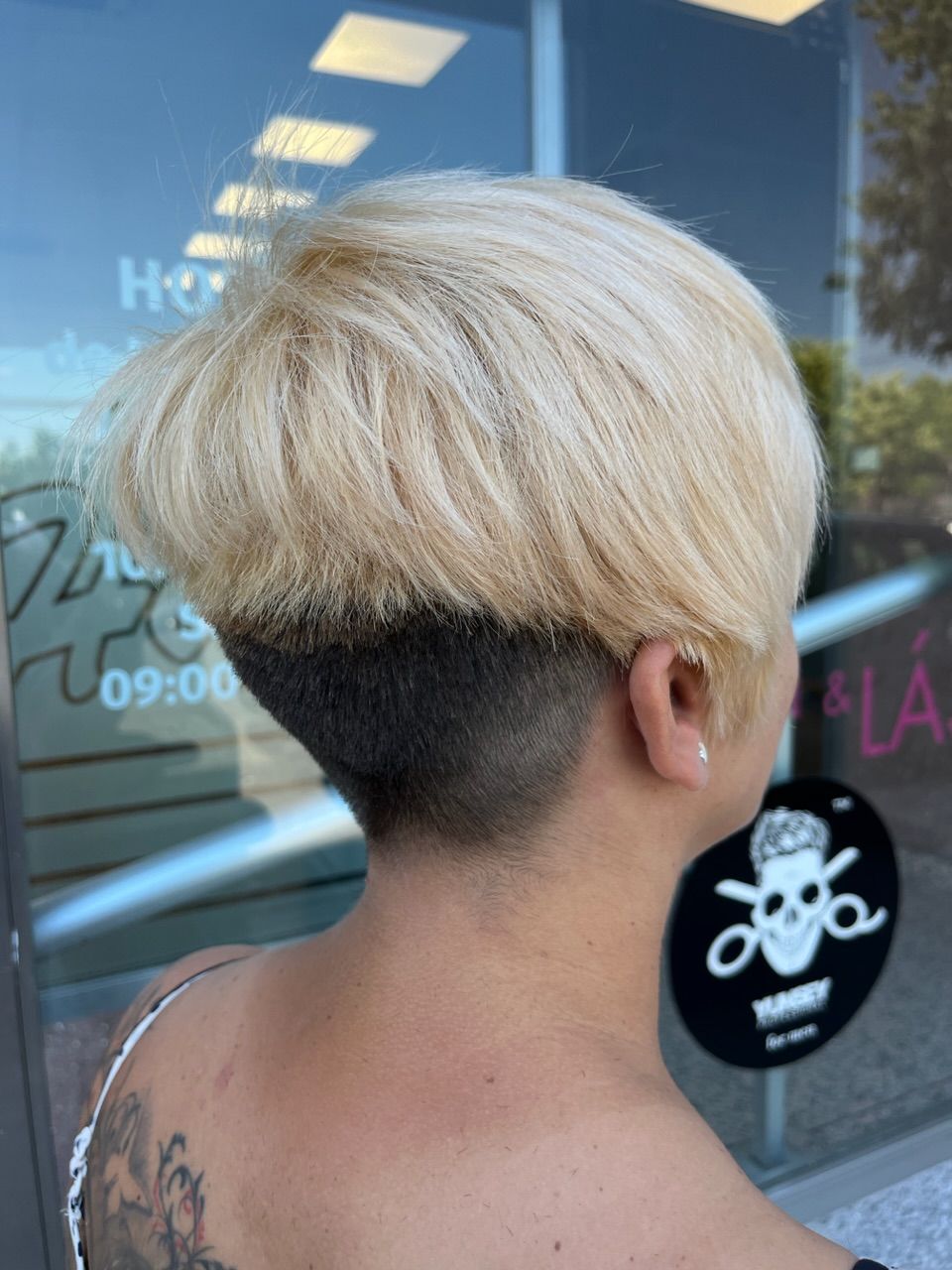 Una mujer con cabello rubio corto tiene un tatuaje en la espalda.