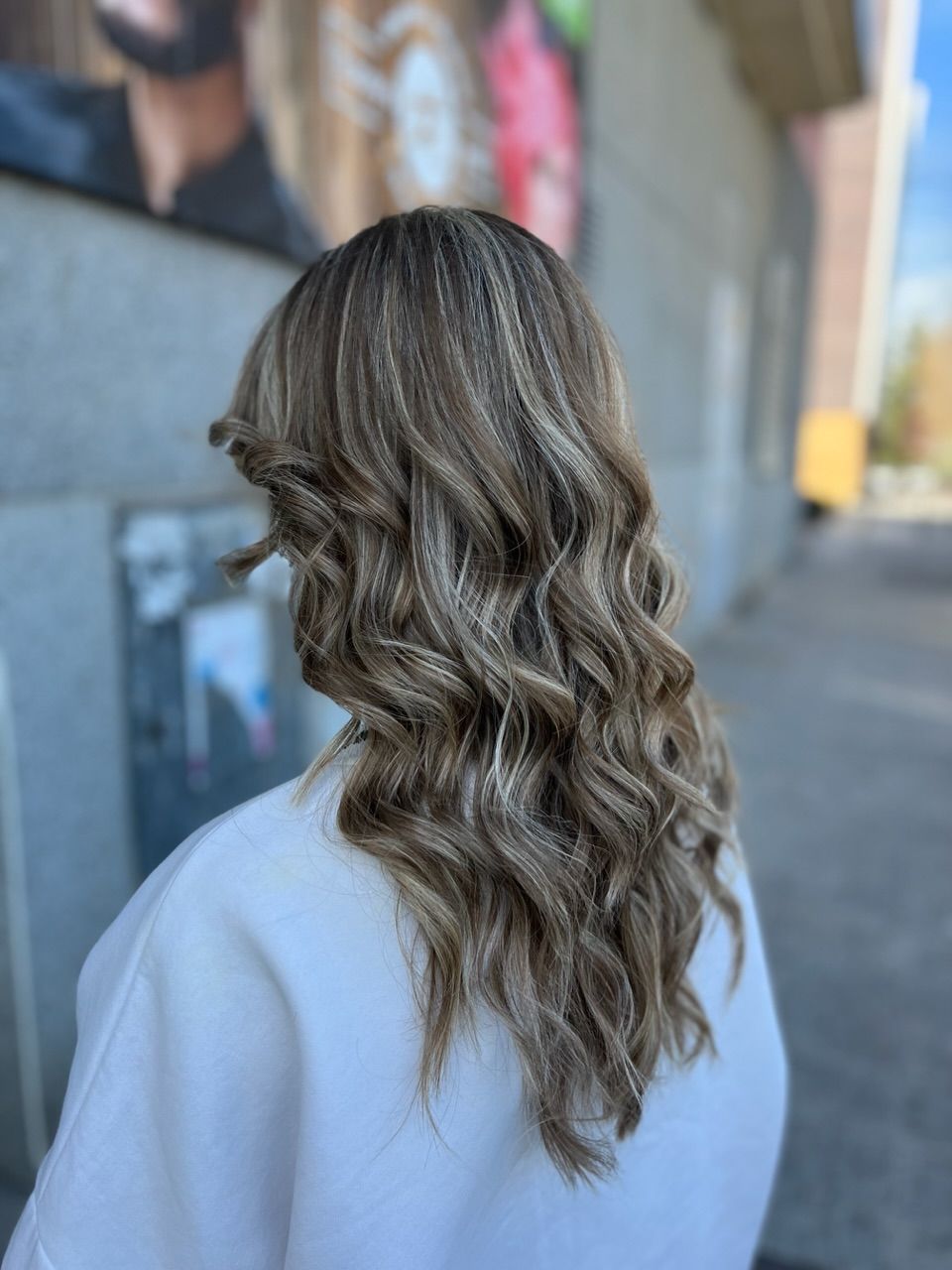 Una mujer con cabello largo y ondulado está parada frente a un edificio.
