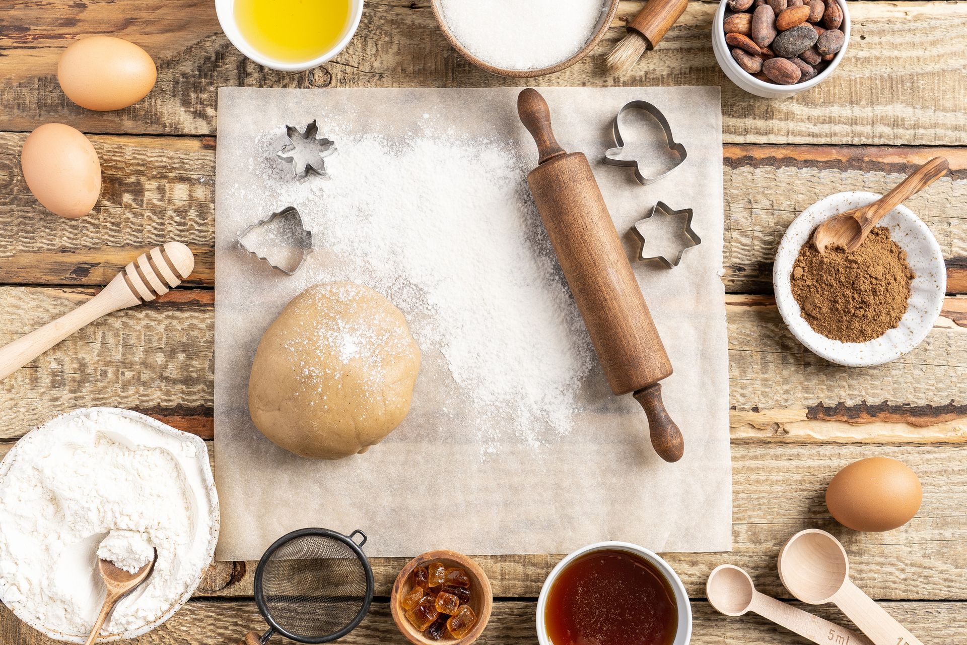 Una mesa de madera cubierta con masa, un rodillo, huevos, azúcar y otros ingredientes para hornear.