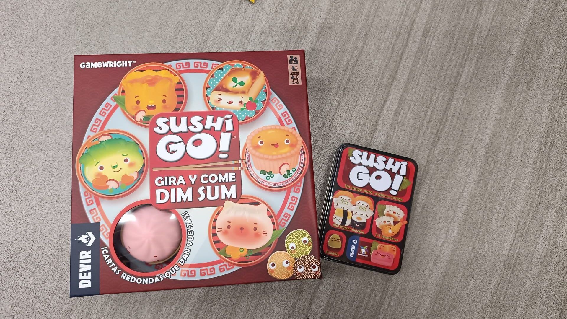 Un juego de sushi go está sentado en una mesa al lado de un juego de dim sum.
