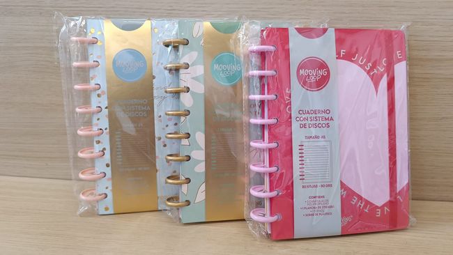 Tres cuadernos están envueltos en plástico y colocados sobre una mesa de madera.