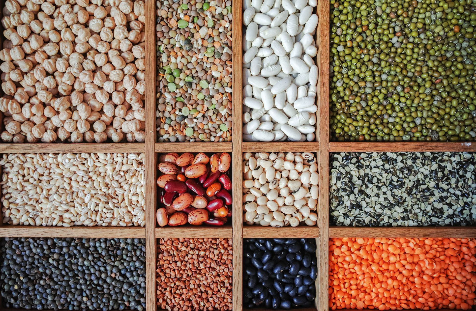 Una caja de madera llena de diferentes tipos de frijoles y granos.