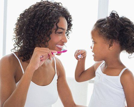 Une femme et une enfant souriantes se brossant les dents les yeux dans les yeux