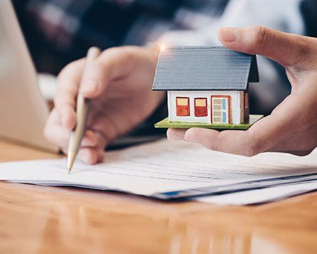 Signature d'un papier d'une main, l'autre main tient une maison miniature