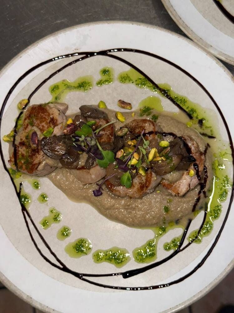 Plato gourmet emplatado con carne sellada, champiñones y salsa verde en un plato blanco con líneas oscuras de glaseado.