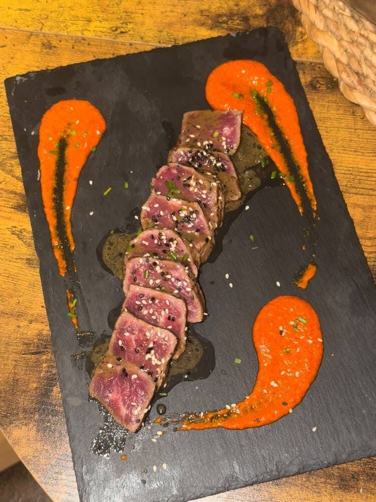 Filete en rodajas sellado sobre un plato de pizarra negra con un chorrito de salsa de naranja alrededor.
