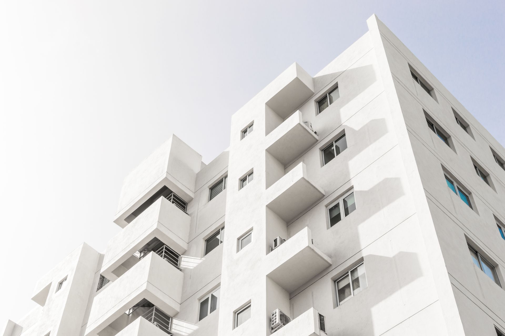 Edificio de apartamentos moderno de color blanco con balcones, contra un cielo azul claro.