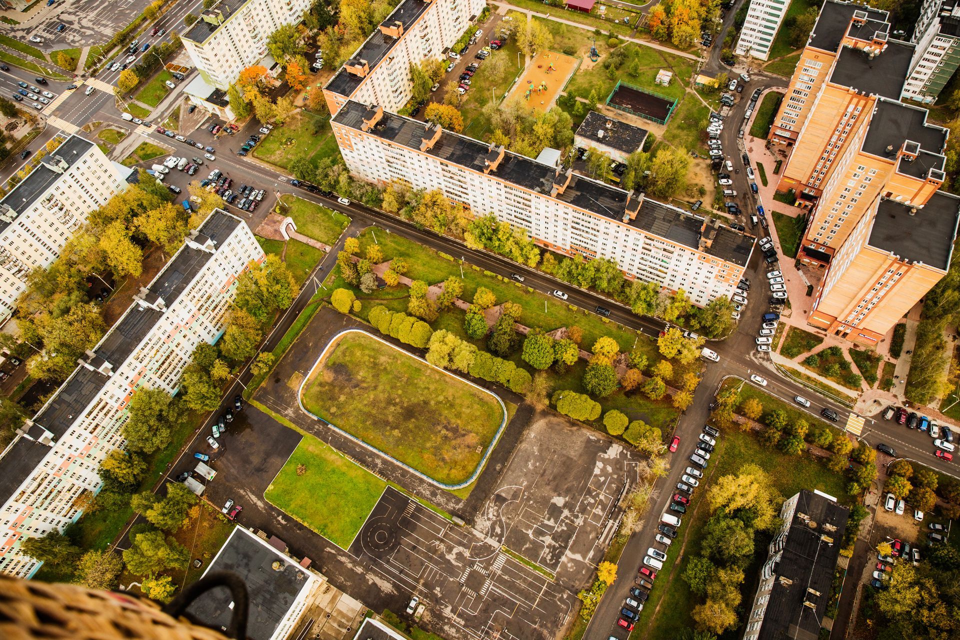Vista aérea de una zona residencial con edificios de departamentos, caminos, árboles y un campo deportivo.