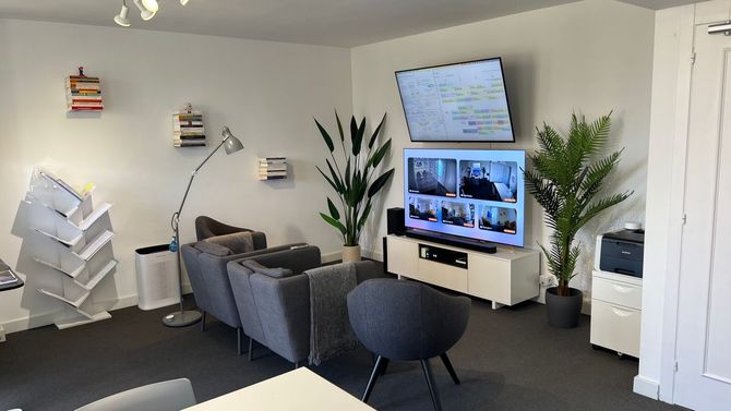 Moderna sala de descanso de oficina con sillas grises, pantallas en la pared, plantas y un expositor blanco