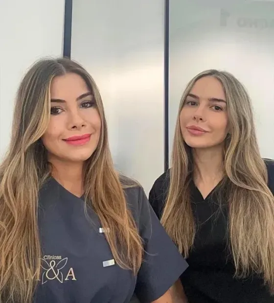 Una mujer con uniforme médico está sentada en un escritorio, sonriendo. Teclado, impresora y ratón blancos.