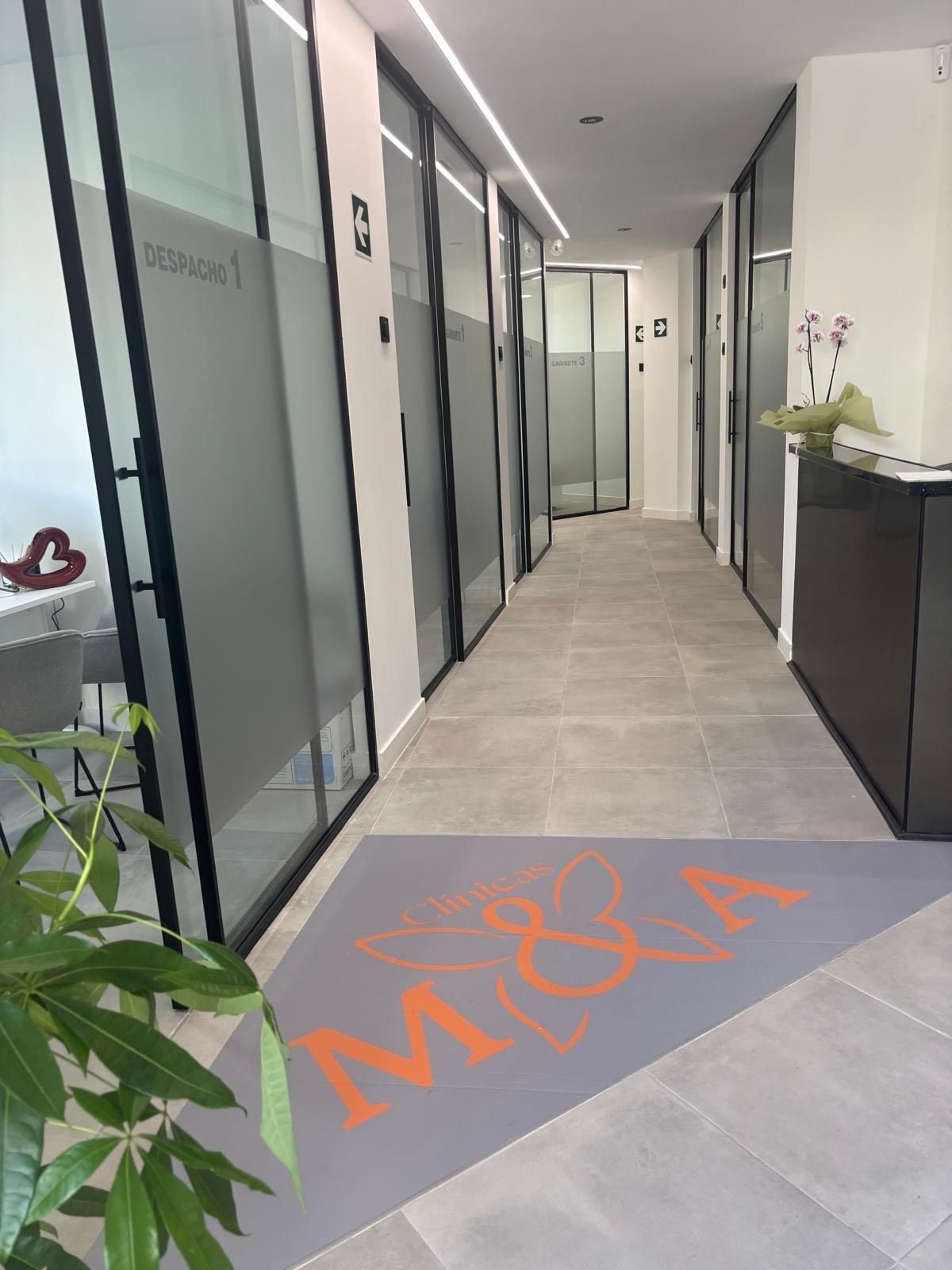 Pasillo largo con oficinas acristaladas. Un felpudo de bienvenida con el logo de