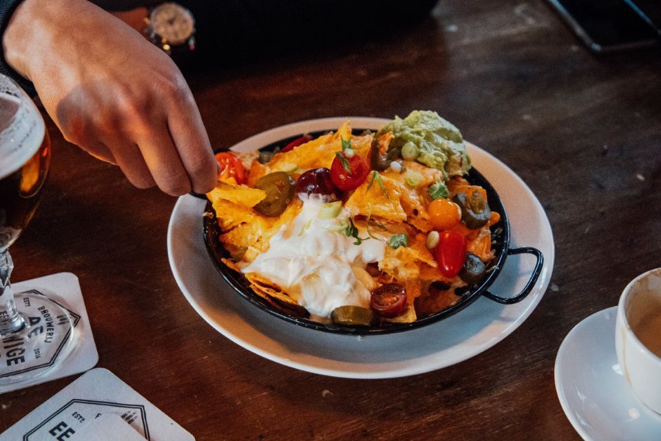 A person is taking a spoonful of nachos from a plate on a table.
