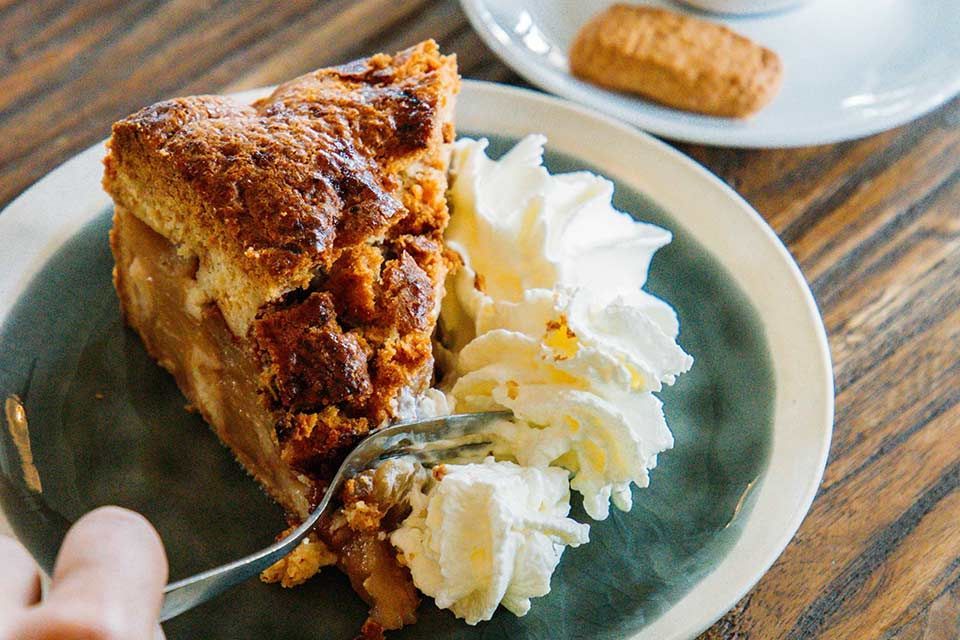 A person is eating a slice of apple pie with whipped cream.