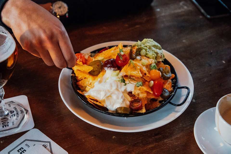 A person is taking a spoonful of nachos from a plate.