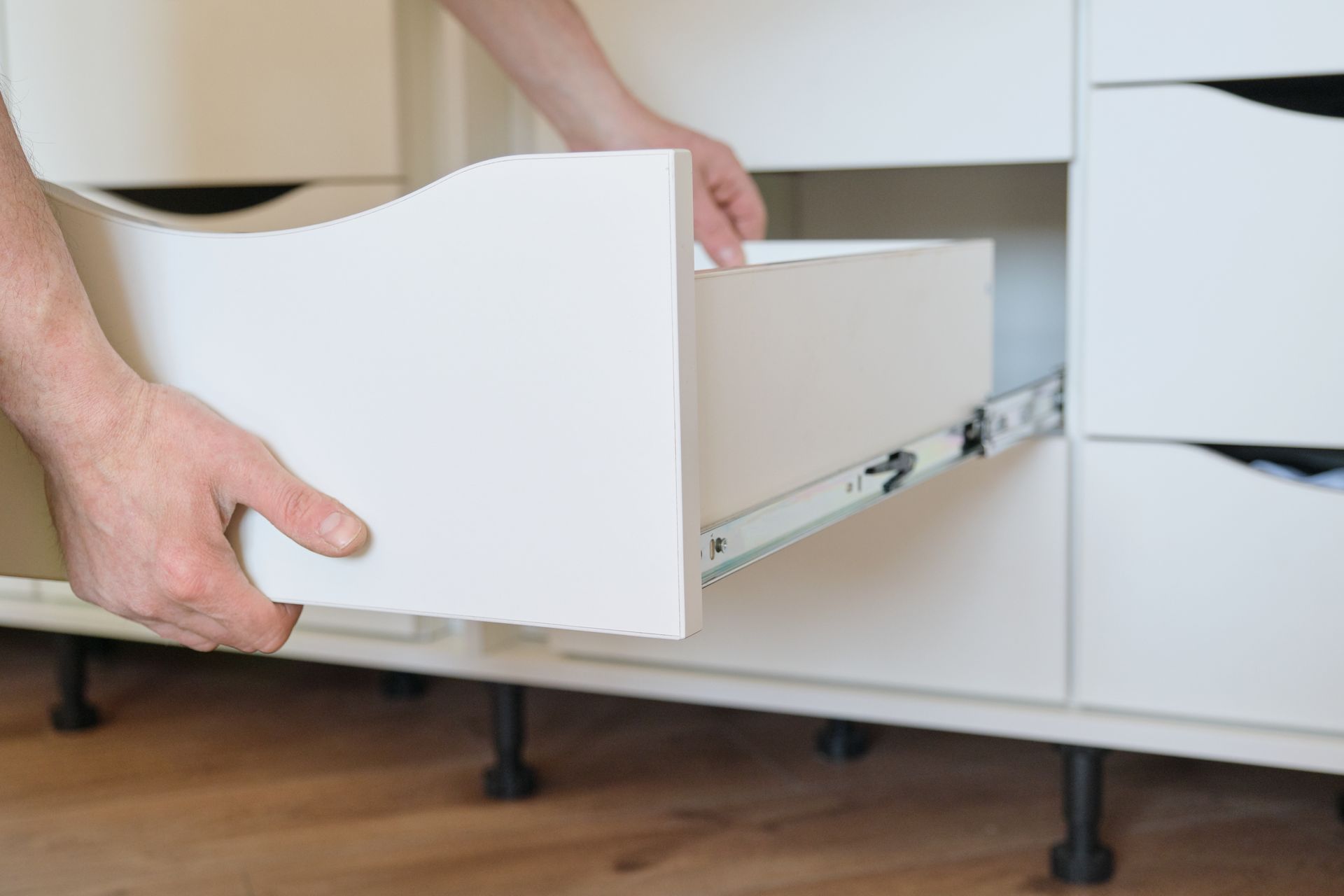 Une personne installe un tiroir blanc dans un meuble.