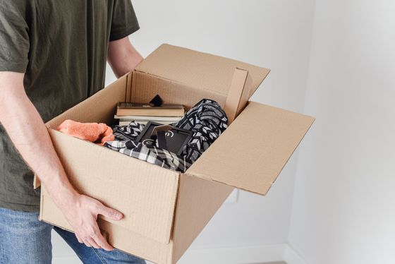 Personne tenant ouverte une boîte en carton remplie de vêtements et de livres.