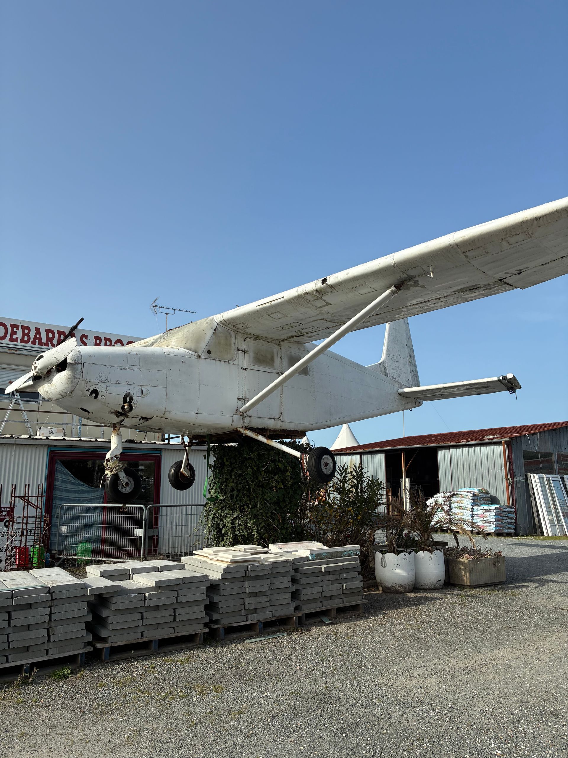 Un avion blanc est stationné au-dessus d'un bâtiment, probablement un magasin ou une entreprise. Ciel d'un bleu éclatant.