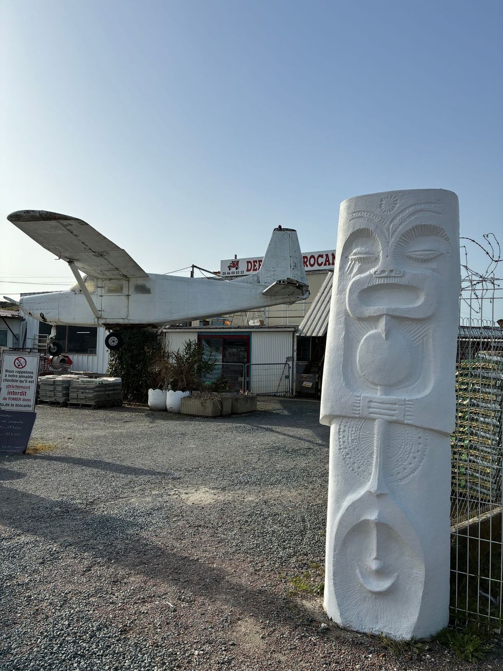 Statue tiki blanche devant un avion usé par le temps et un ciel bleu.