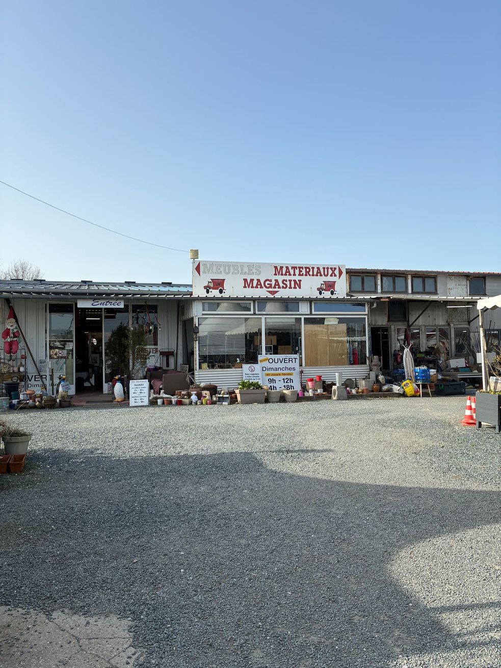 Façade de magasin avec une enseigne en lettres rouges, entourée de gravier, sous un ciel d'un bleu éclatant.