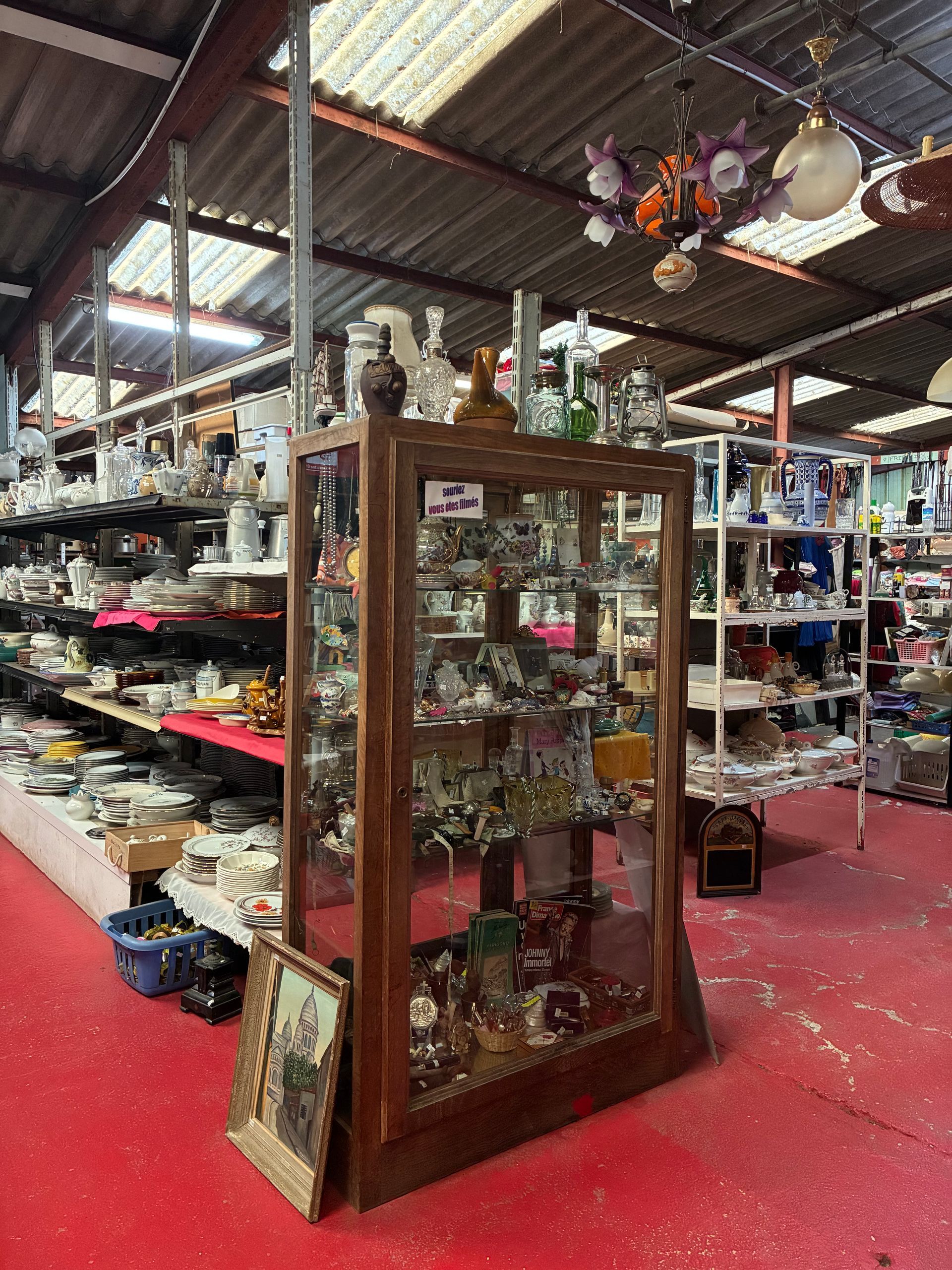 Intérieur encombré d'une boutique d'antiquités, avec vitrines et étagères remplies d'objets divers. Sol rouge.