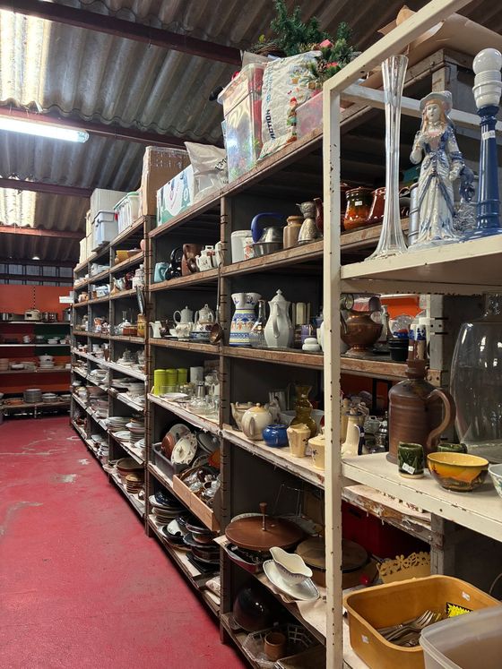 Des étagères dans un entrepôt remplies d'articles divers, notamment de la céramique et de la verrerie, avec un sol rouge.