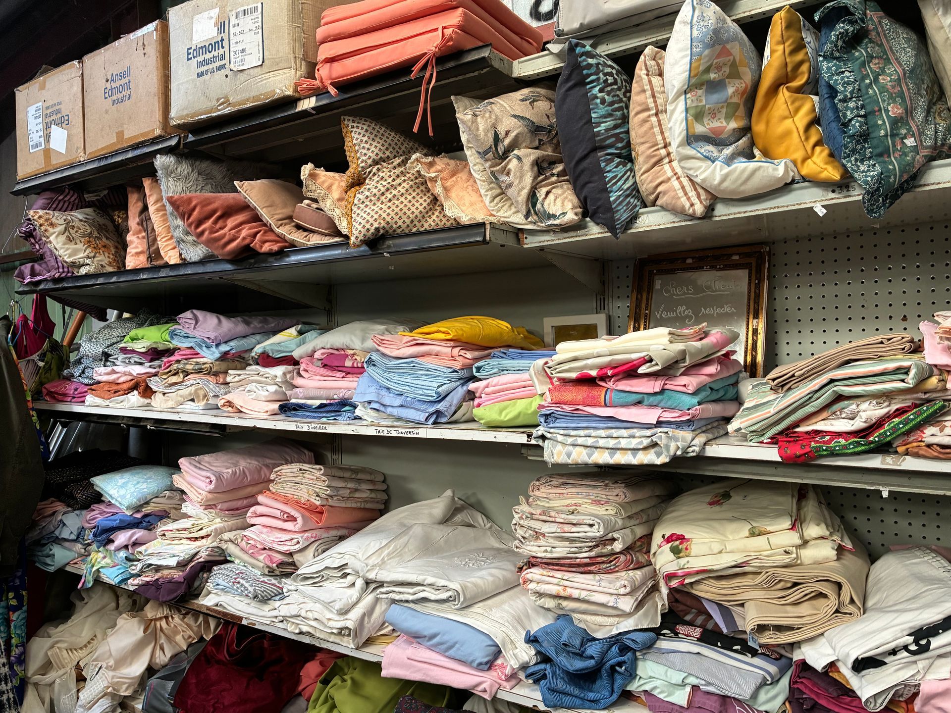 Des étagères débordant de piles de tissus et de coussins de couleurs et de motifs variés.